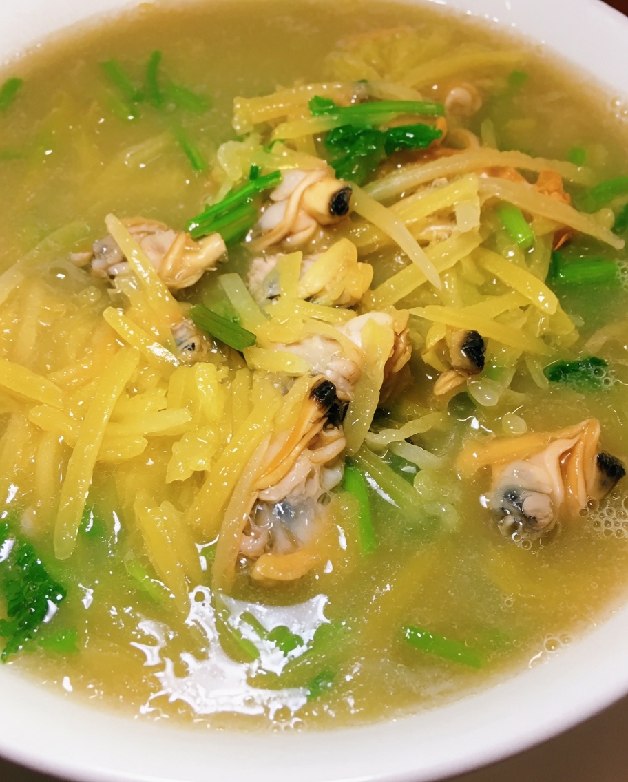 Un primer plano de cilantro fresco picado siendo espolvoreado en una olla burbujeante de sopa de patata y almejas.