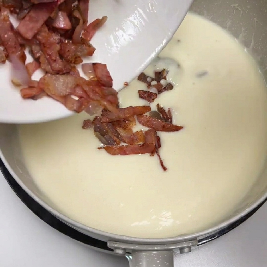 Bacon y cebolla salteados siendo añadidos desde un plato a la sopa cremosa de patata.