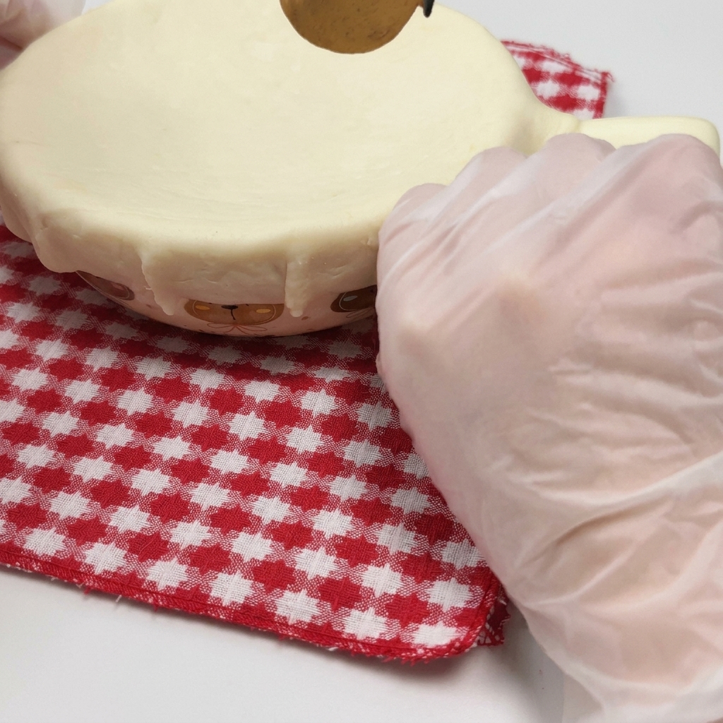 Una mano enguantada presionando una lámina de hojaldre sobre el borde de un cuenco apto para horno para sellarlo.