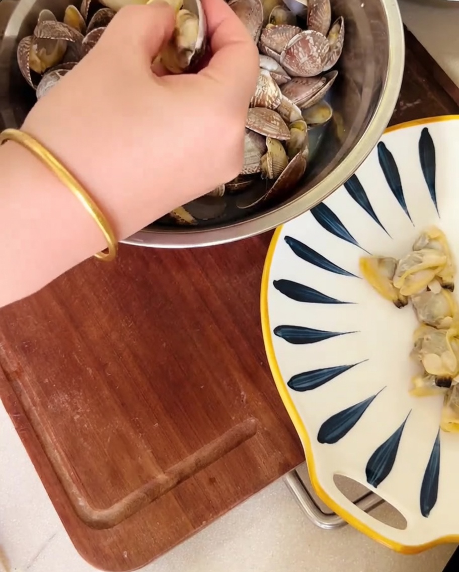 Una mano retirando carne de almeja de las conchas sobre un tazón, con el caldo siendo reservado.