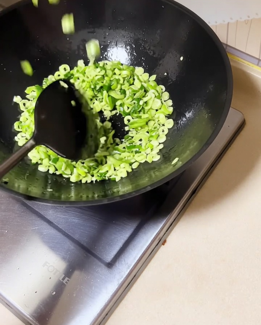 Judías verdes picadas siendo removidas en el wok con cebollinos salteados.