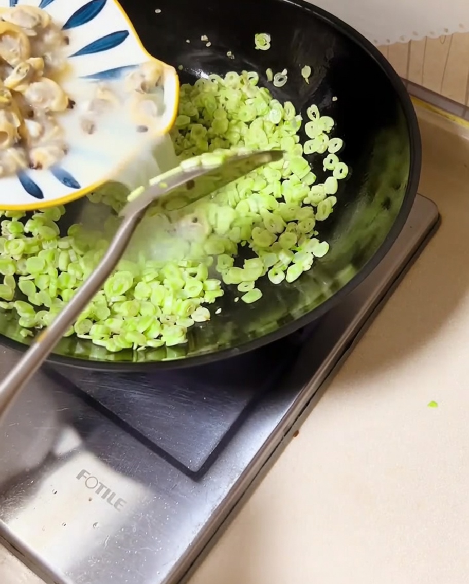Carne de almeja y caldo siendo vertidos en el wok con las judías verdes.