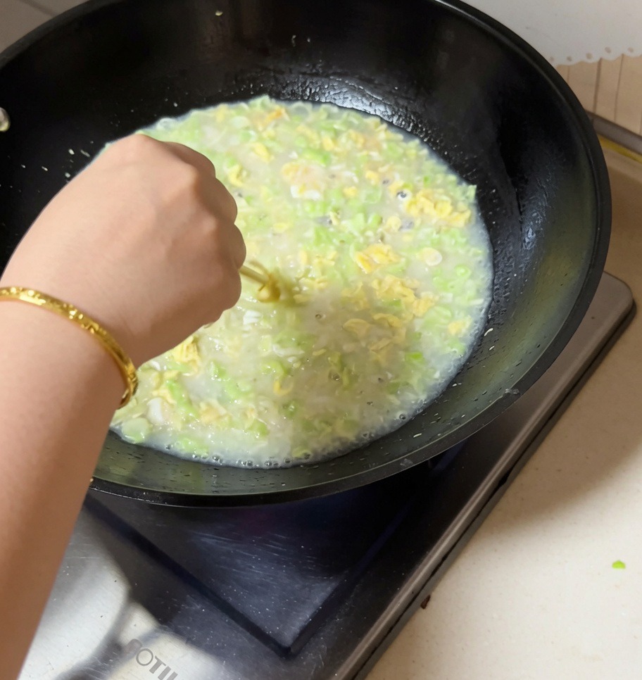 Una mano removiendo un wok burbujeante de sopa de almejas, judías verdes y huevo con palillos.