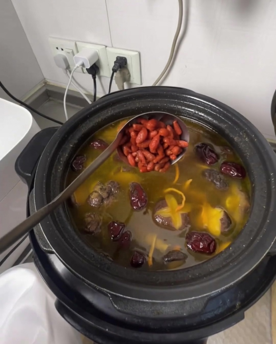 Un cucharón añadiendo bayas de goji a la aromática sopa de pollo.
