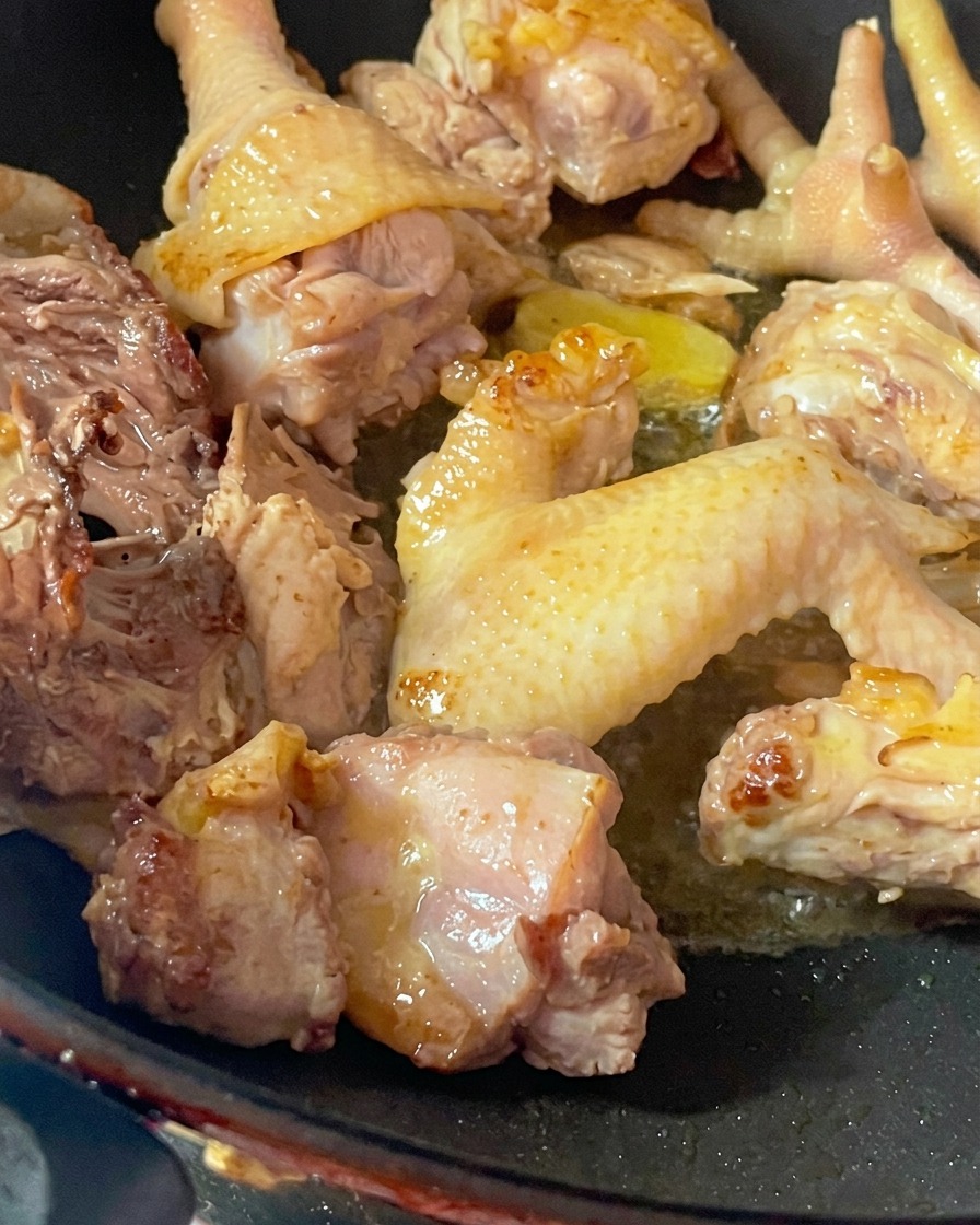 Trozos de gallina vieja siendo sofritos en un wok caliente para eliminar la humedad.