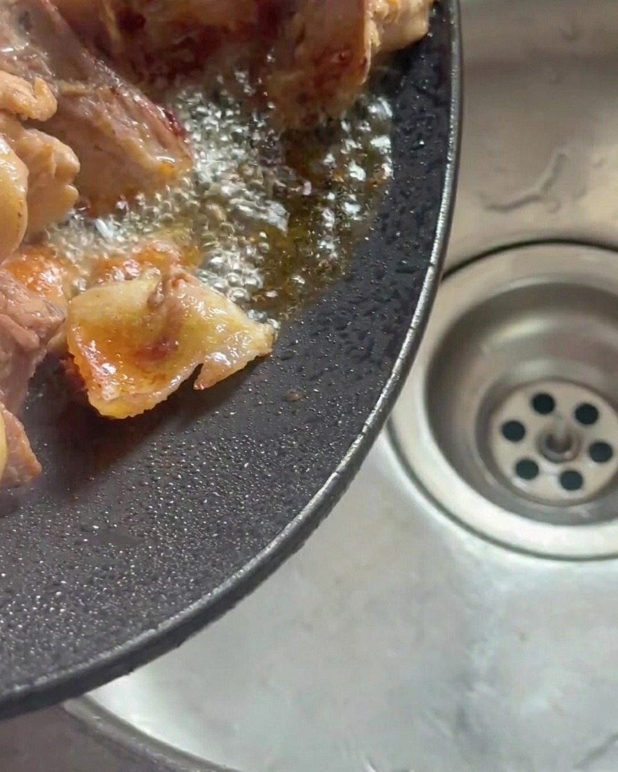 Wok inclinado vertiendo el aceite de pollo acumulado en un fregadero.