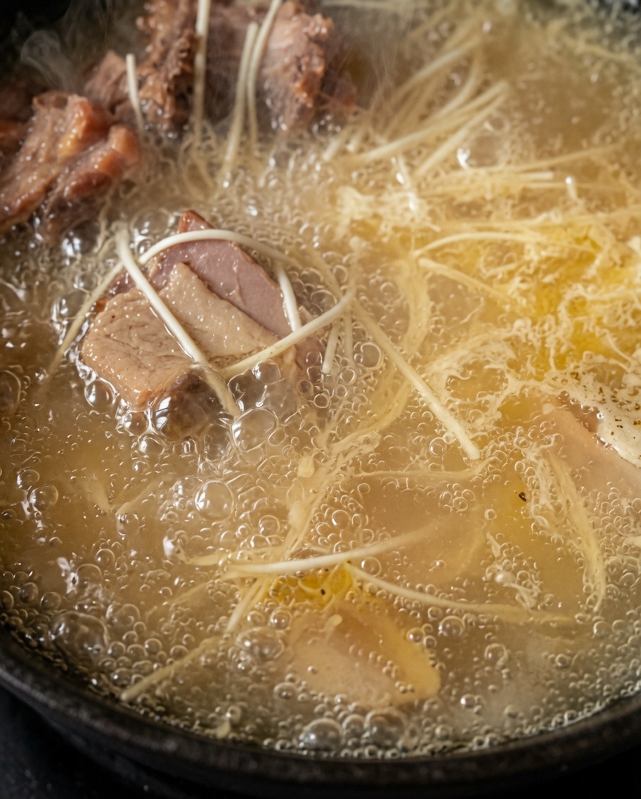 Fideos cocinándose en la sopa de pollo rica y blanca.