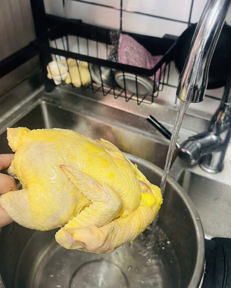 Una mano sosteniendo una gallina entera bajo el grifo, lista para colocar en la olla.