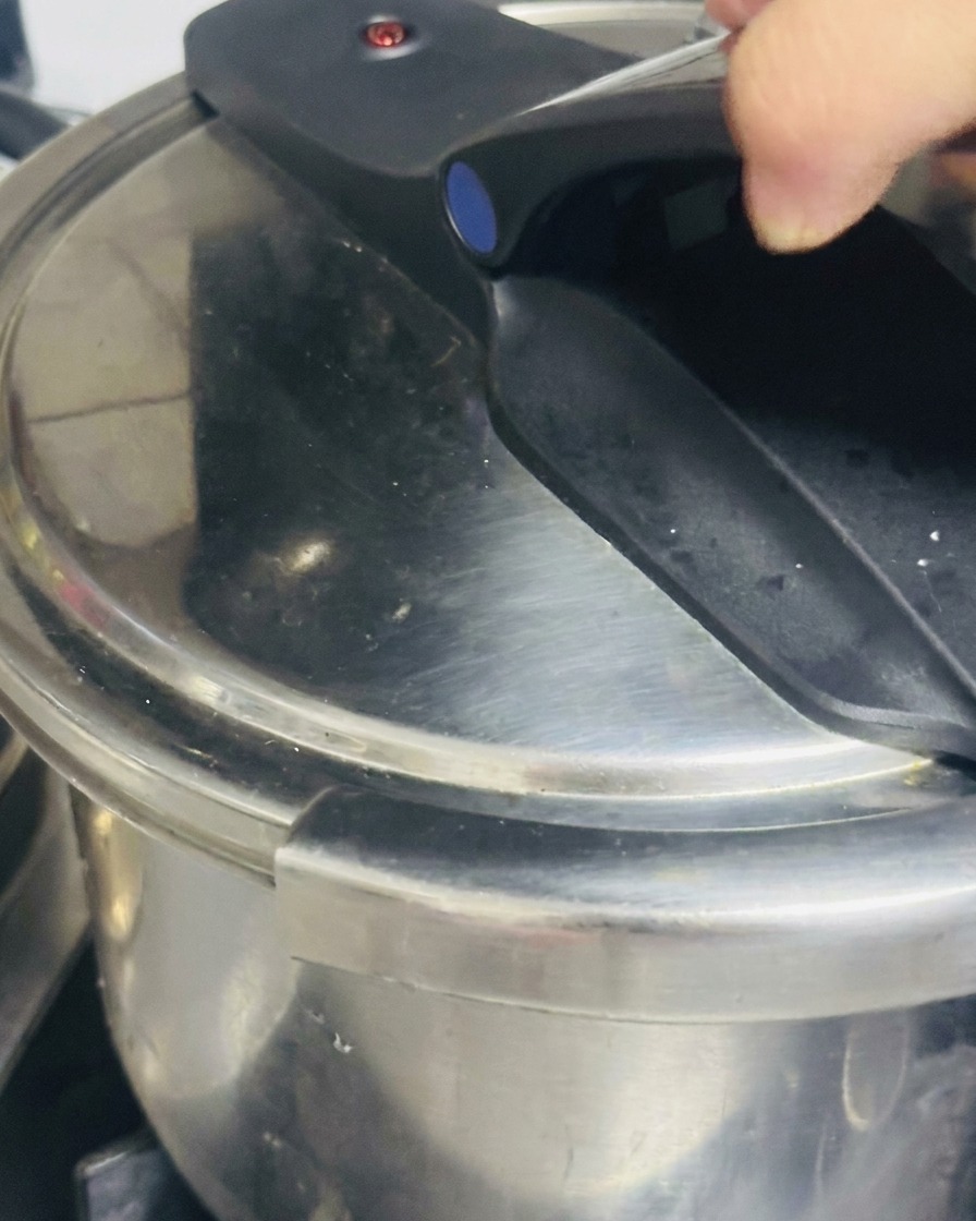 Una mano cerrando el mango de una olla a presión de acero inoxidable.