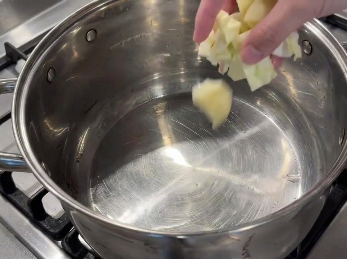 Mano añadiendo verduras picadas en una olla grande con aceite.