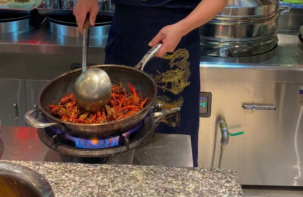 Chef salteando cangrejos de río rojos en un wok grande sobre una llama abierta.