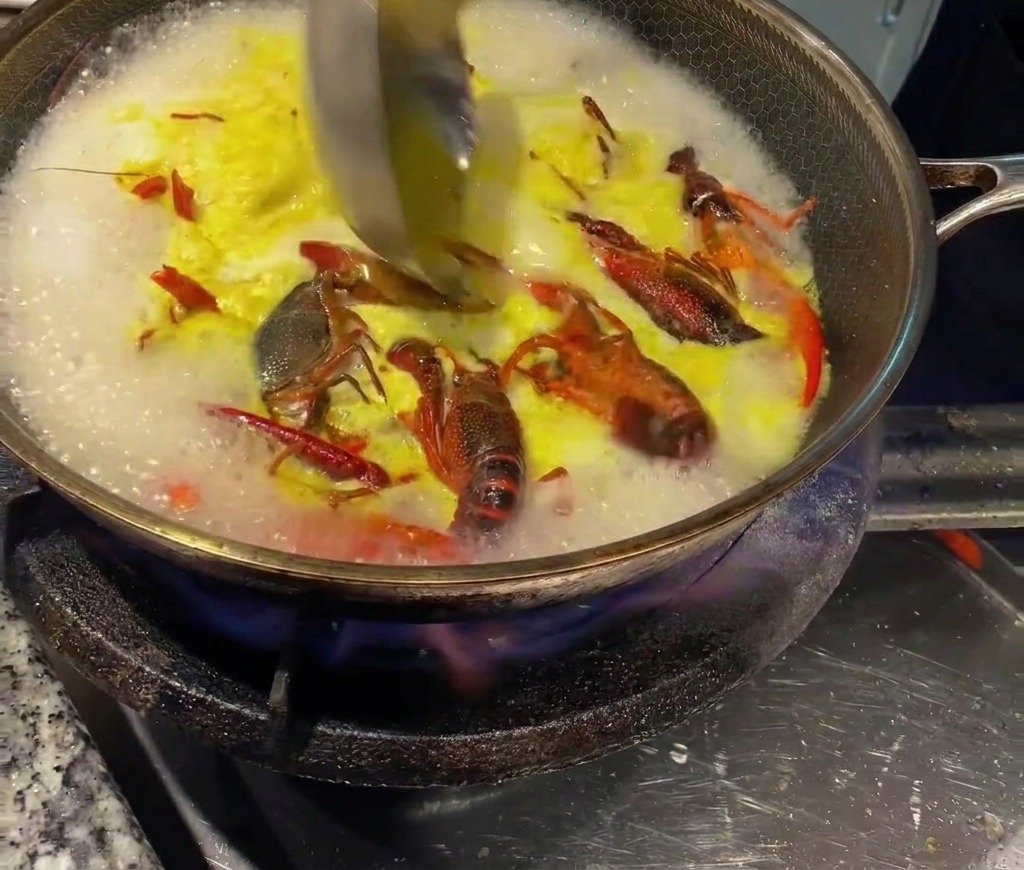Un cucharón mezclando caldo de pollo concentrado en el caldo caliente de los cangrejos.