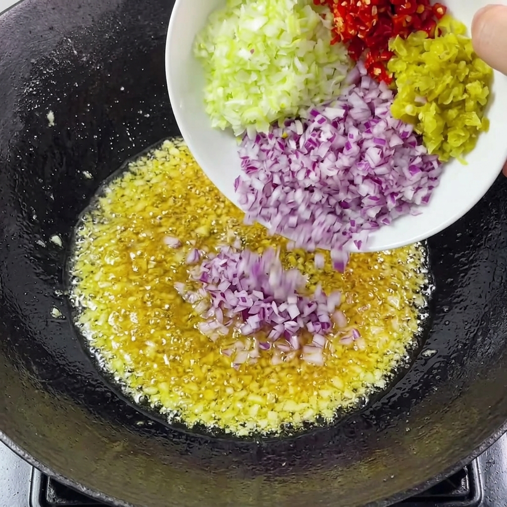 Cebollas, cebollinos y chiles picados siendo añadidos al ajo en el wok.