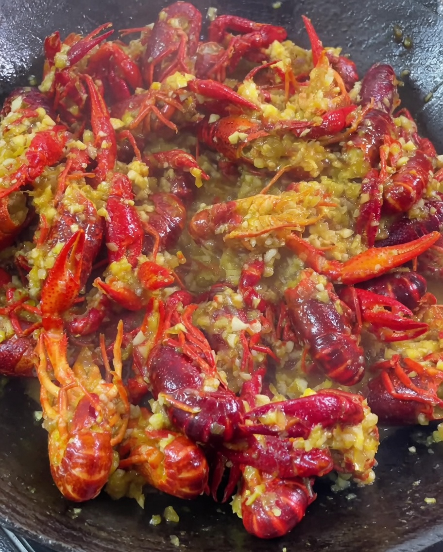 Ajo picado, curry en polvo y sazones siendo añadidos a un wok con los cangrejos cocinándose.