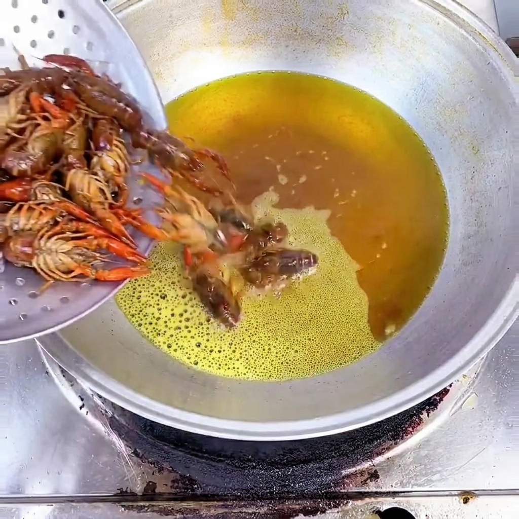 Cangrejos de río crudos vertidos en un wok con aceite caliente.