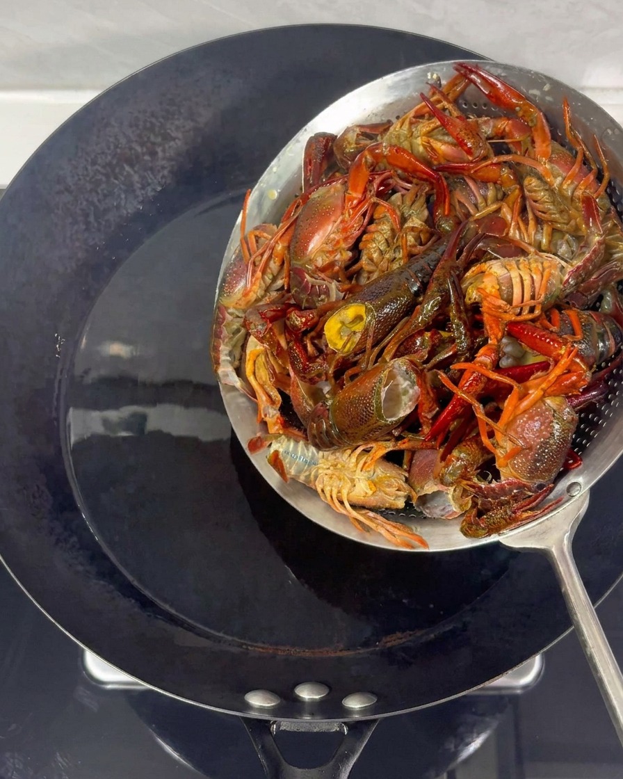 Cangrejos siendo retirados del aceite caliente en un wok usando un colador metálico.