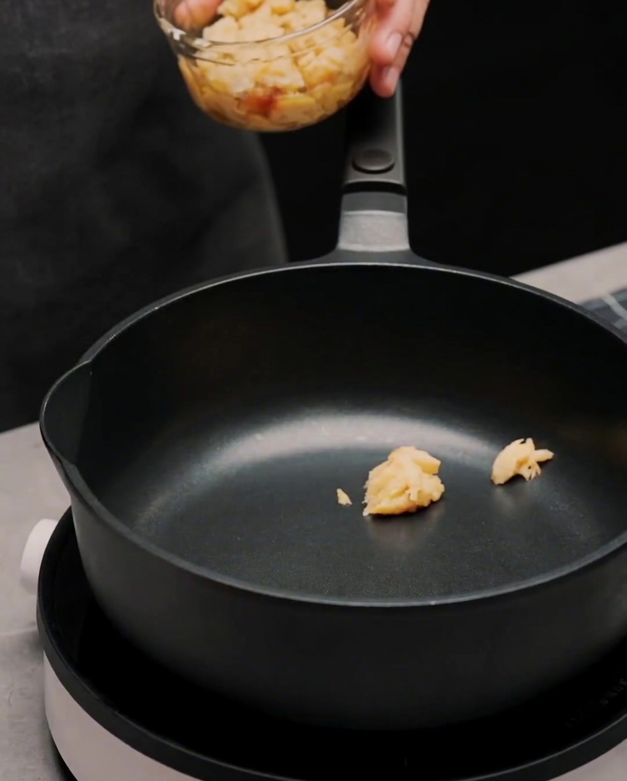 Aceite de oliva y hojuelas de chile siendo añadidos a la sartén que contiene la pasta de ajo.