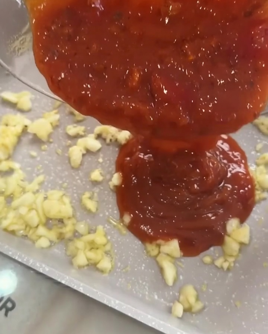 Salsa de carne y tomate vertiéndose sobre el ajo sofrito en una sartén.
