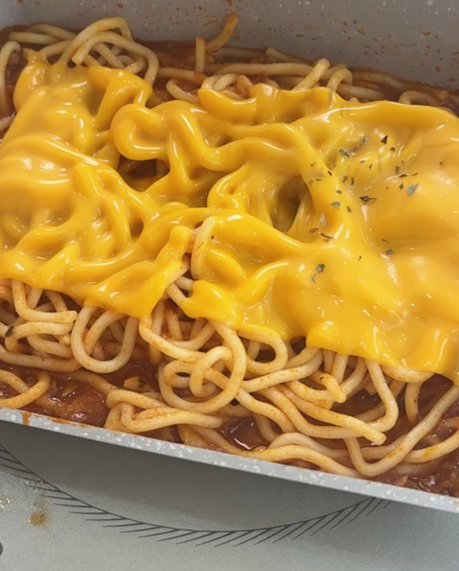 Espaguetis cubiertos con queso derretido y un toque de perejil seco.