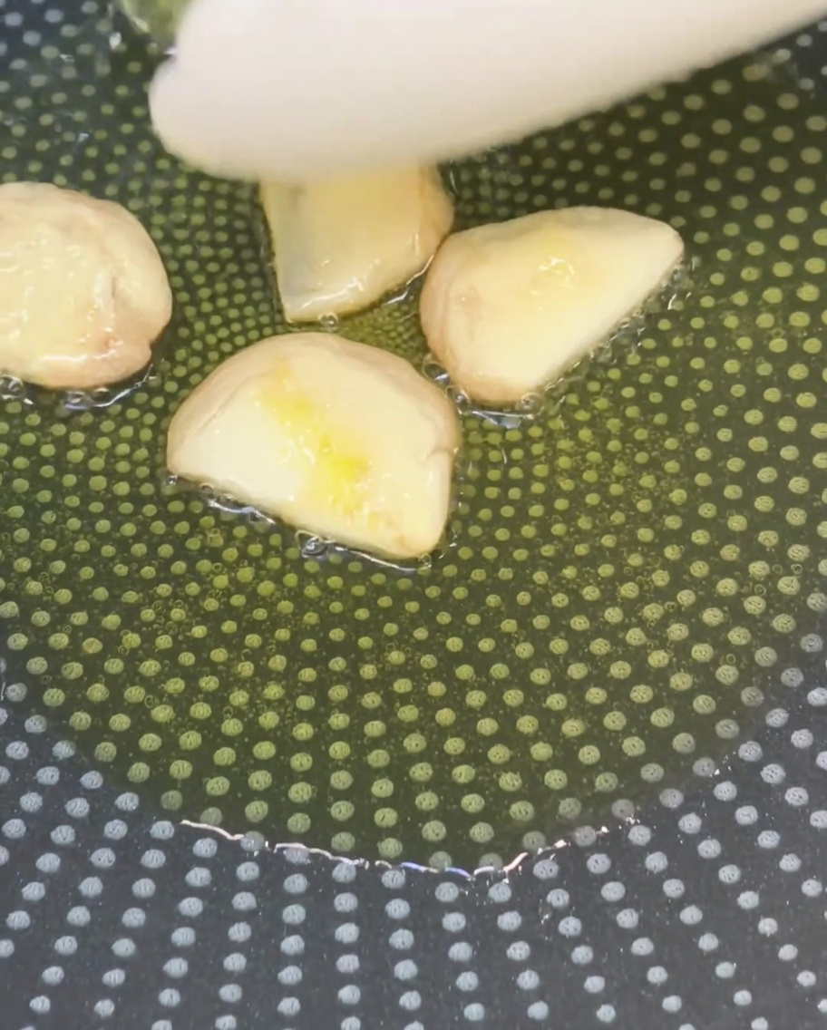 Dientes de ajo aplastados friéndose en aceite de oliva en una sartén antiadherente.