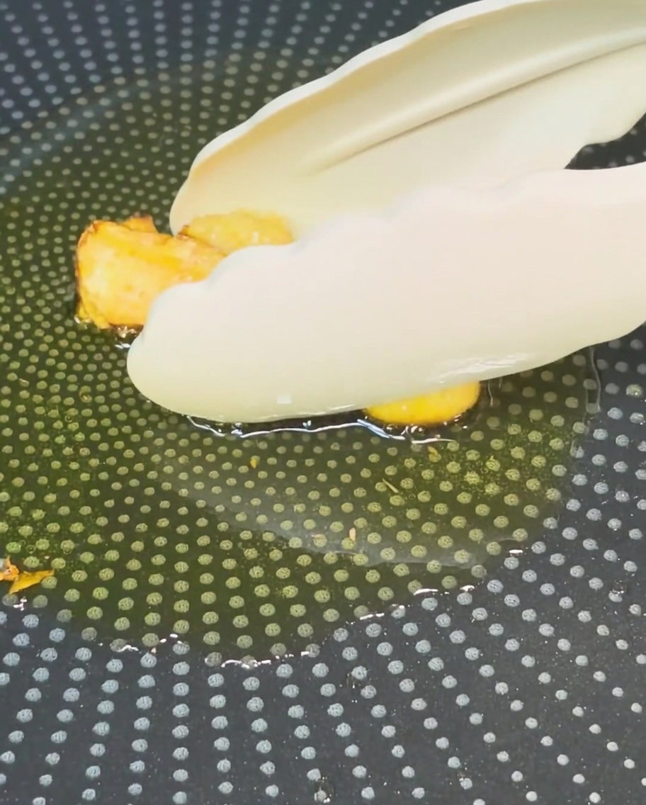 Pinzas retirando el ajo frito dorado del aceite en una sartén.