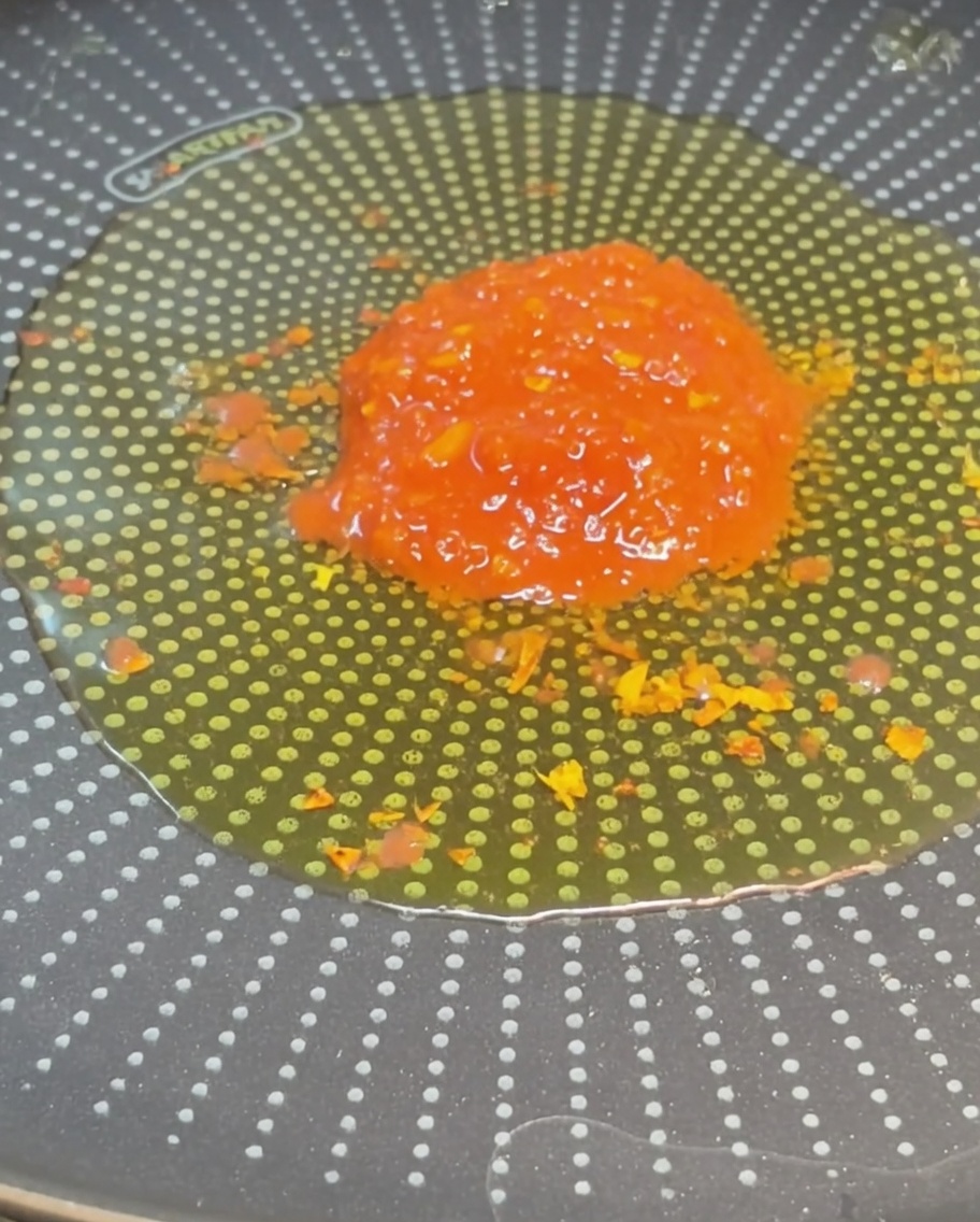 Un montón de tomates cortados en dados grandes y de color rojo brillante en el centro de una sartén llena de aceite de oliva condimentado.