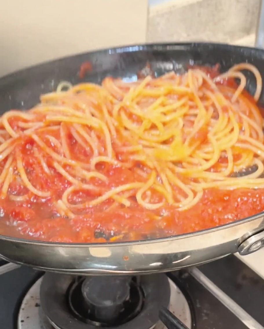 Espaguetis mezclados con pinzas en una sartén, completamente cubiertos de una vibrante salsa de tomate roja.
