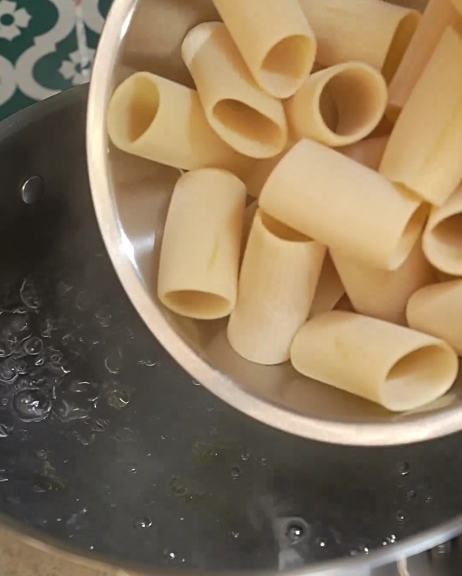 Pasta rigatoni seca cayendo en una olla con agua hirviendo vigorosamente.