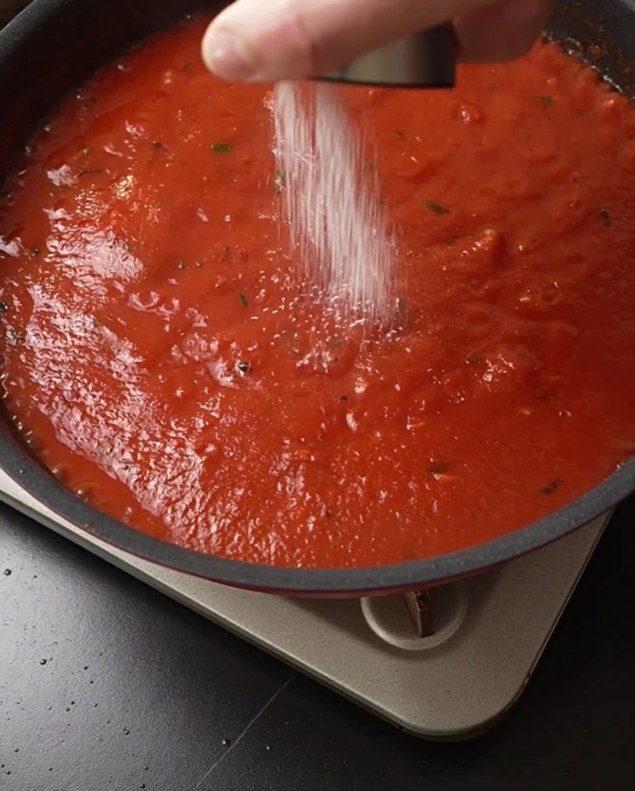 Sal espolvoreándose sobre una rica salsa de tomate roja que hierve a fuego lento.