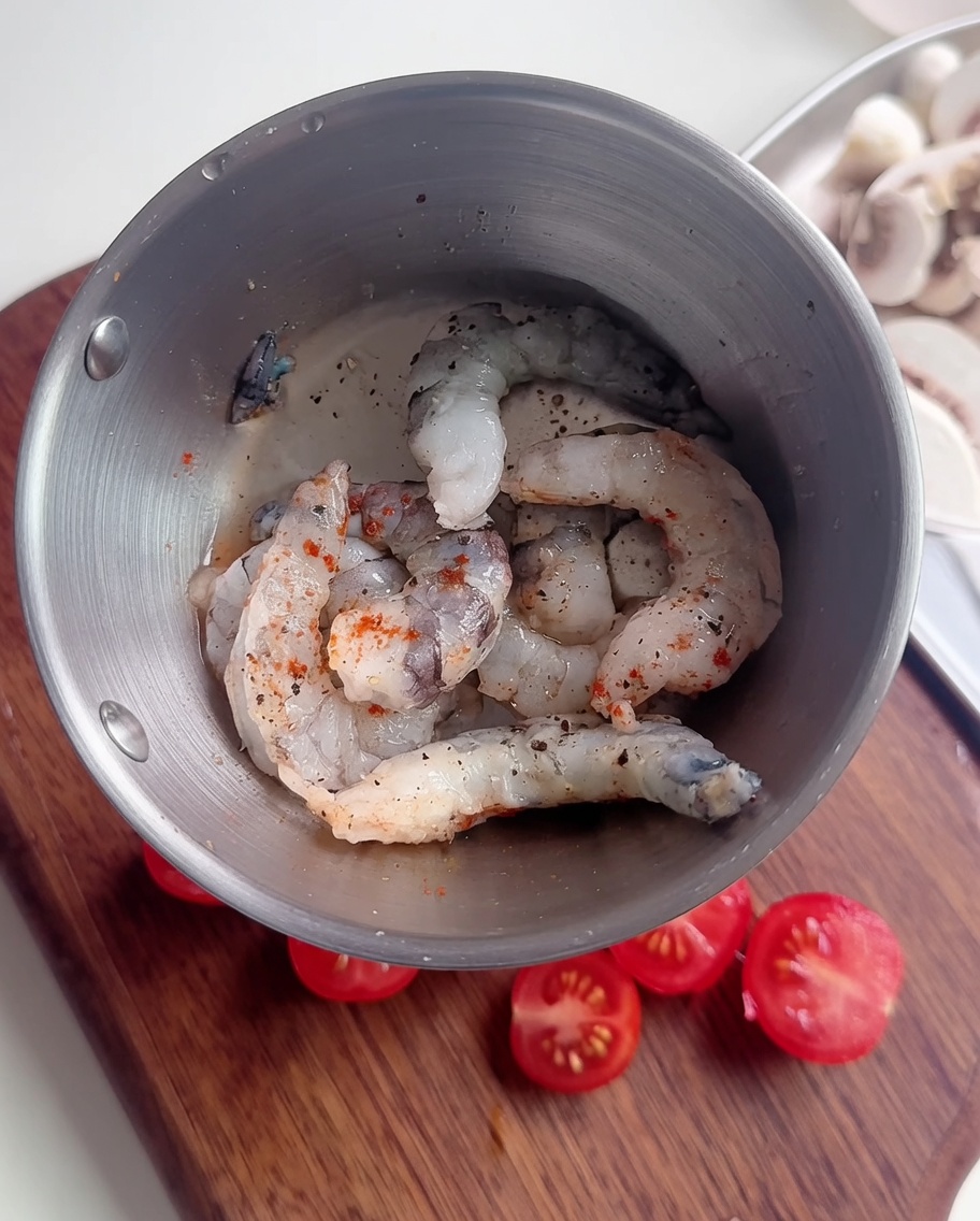 Primer plano de gambas crudas en un bol metálico sazonadas con pimienta negra, chile en polvo y una fina capa de almidón.