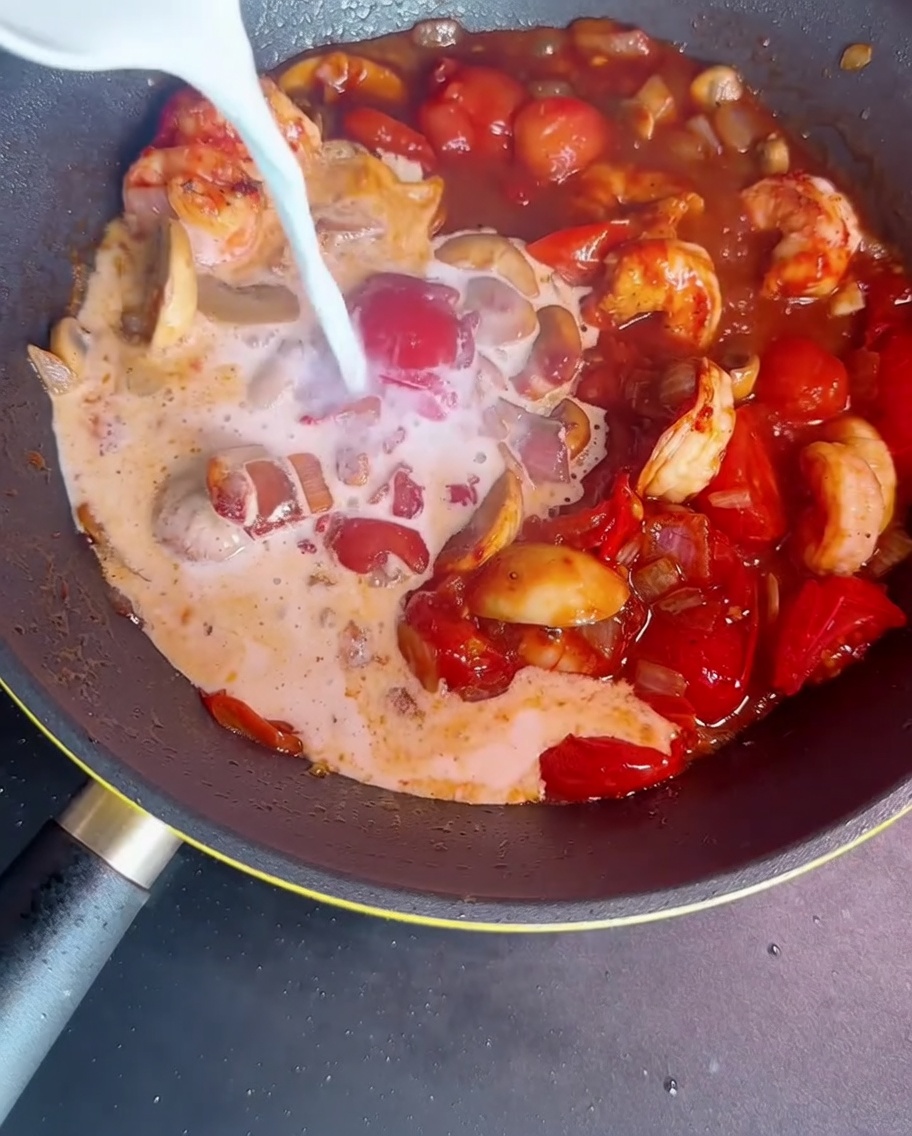 Leche y almidón siendo añadidos a la sartén con los ingredientes para espesar la salsa.