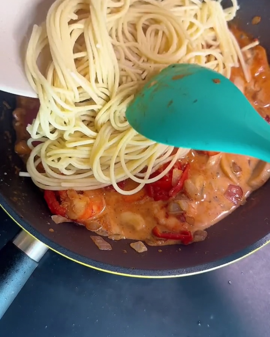 Espaguetis mezclándose en la sartén con la salsa cremosa de gambas y champiñones.