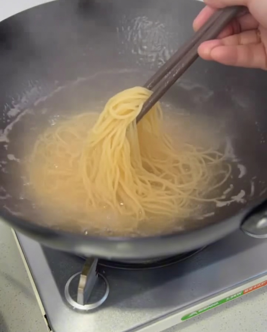 Espaguetis cocidos siendo retirados de la olla para escurrir.