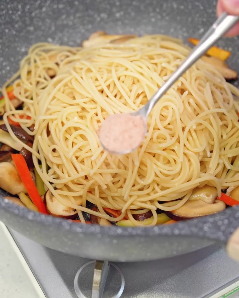 Una cucharadita de sal siendo espolvoreada sobre la pasta en la sartén.