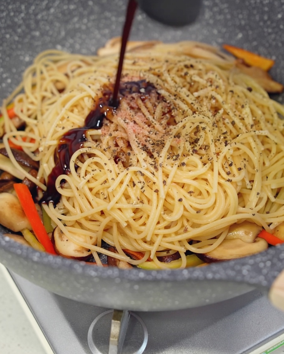 Salsa de ostra vegana siendo vertida sobre la mezcla de pasta y setas.