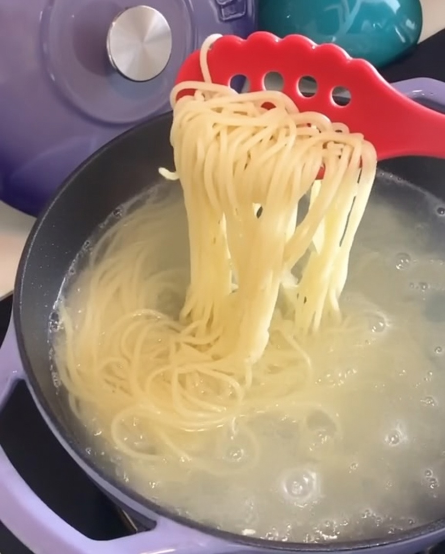 Espaguetis cocidos siendo retirados de la olla con una cuchara roja para pasta.
