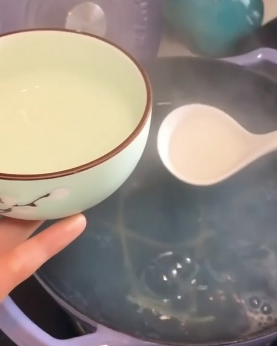 Un pequeño cuenco decorativo llenándose con agua caliente y turbia de cocer la pasta usando un cazo blanco.