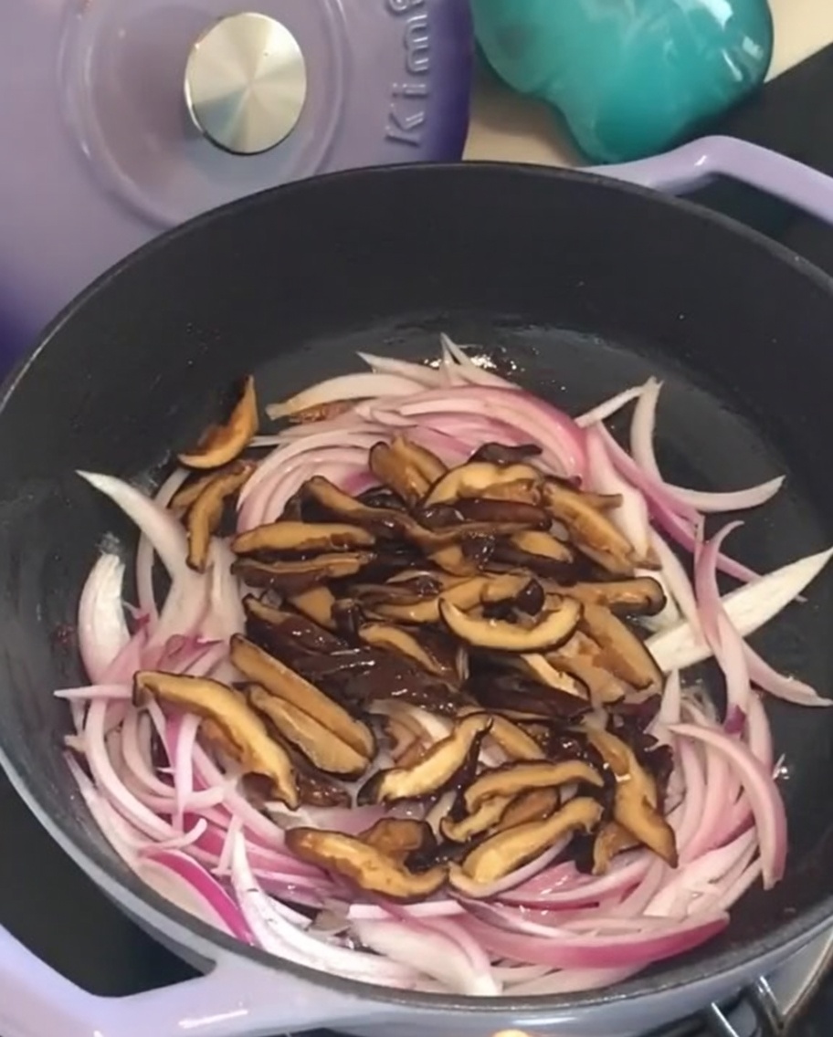 Setas shiitake en láminas colocadas sobre las cebollas rojas en una sartén morada.