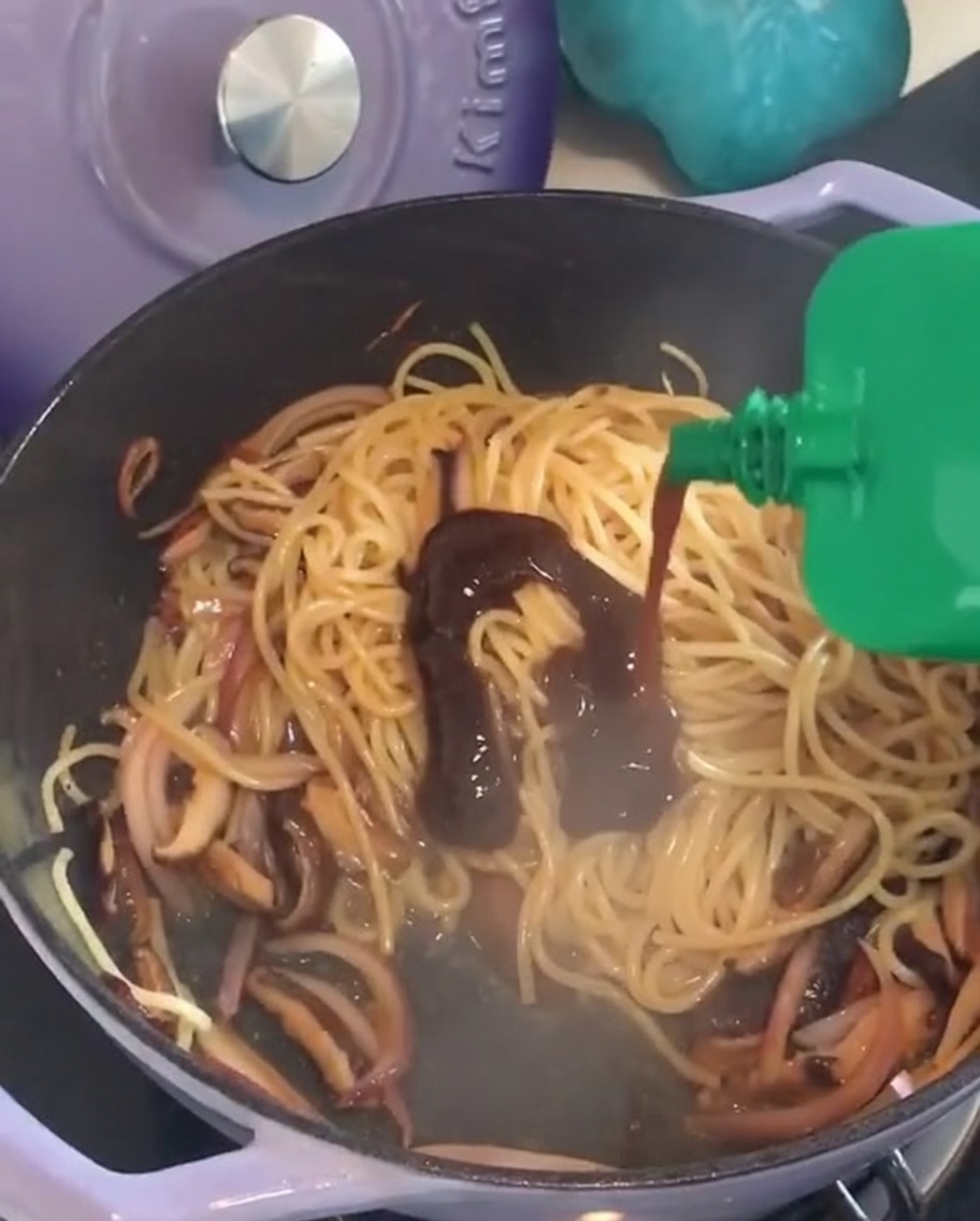 Exprimiendo un paquete verde de salsa de pimienta negra directamente sobre una sartén de espaguetis salteados.
