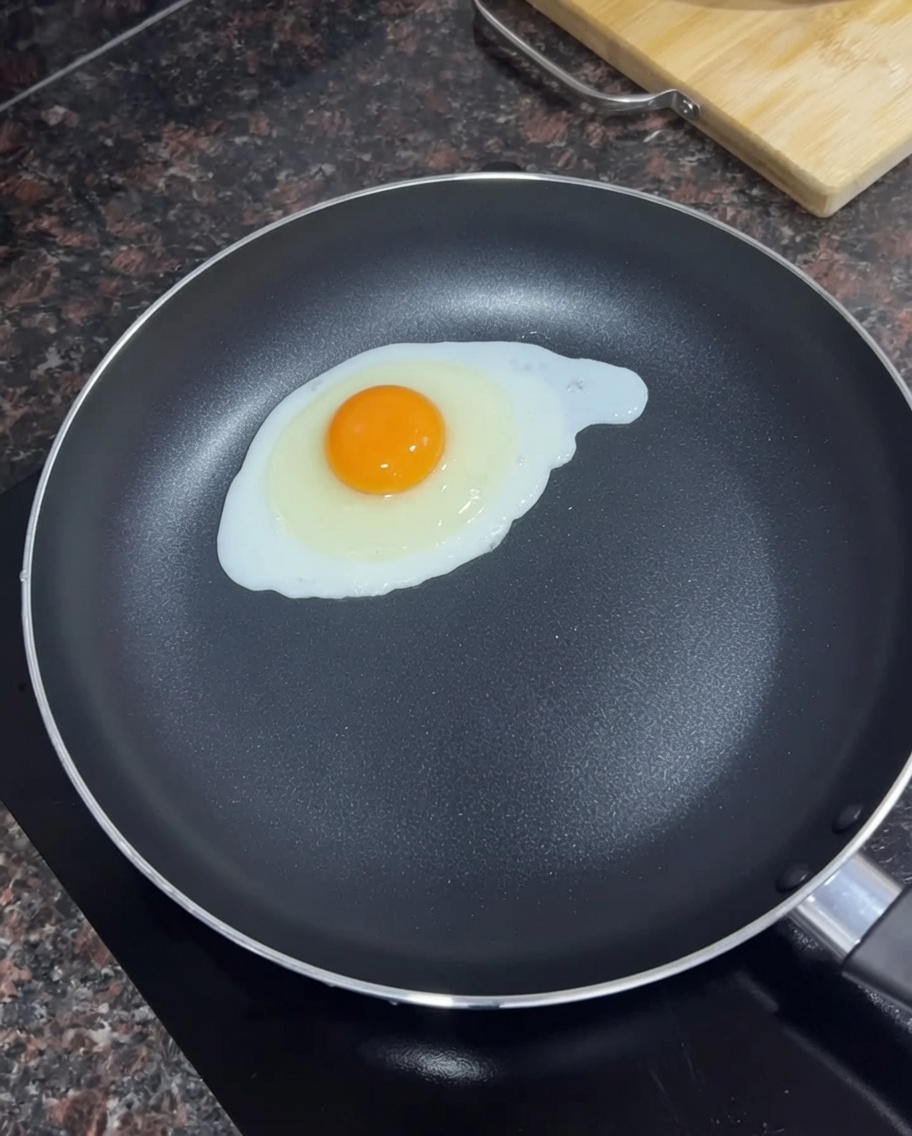 Un solo huevo friéndose en una sartén negra con mantequilla derretida.