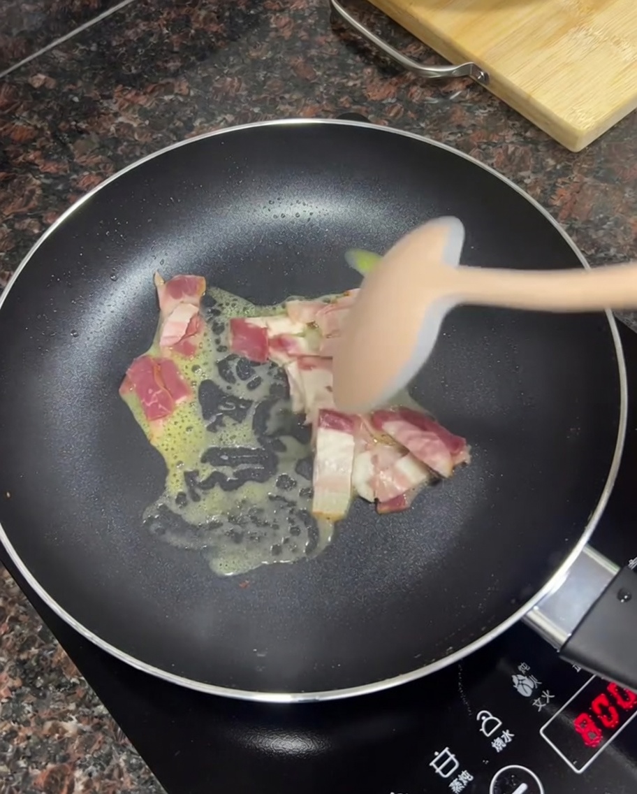 Trocitos de tocino friéndose en mantequilla derretida en una sartén.