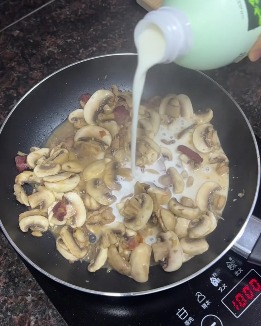 Leche siendo vertida en una sartén con champiñones y tocino salteados.