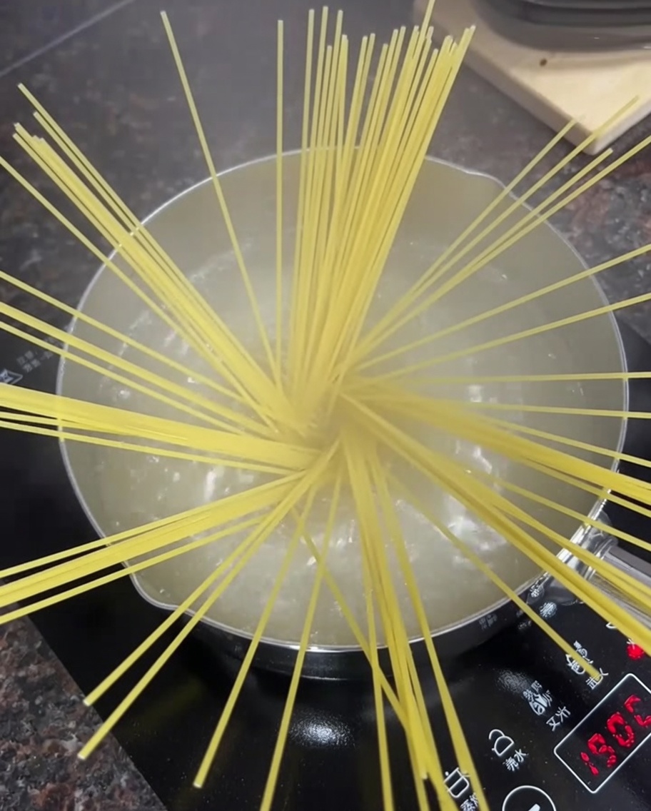 Fideos de espagueti secos extendidos en una olla con agua hirviendo en una estufa.