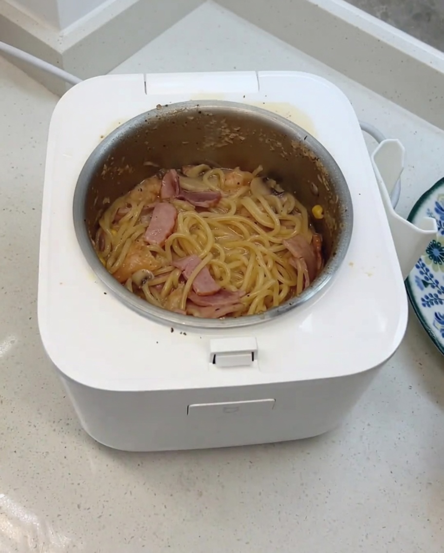 Los espaguetis cremosos con champiñones siendo mezclados con queso y cubitos lácteos en la olla arrocera.