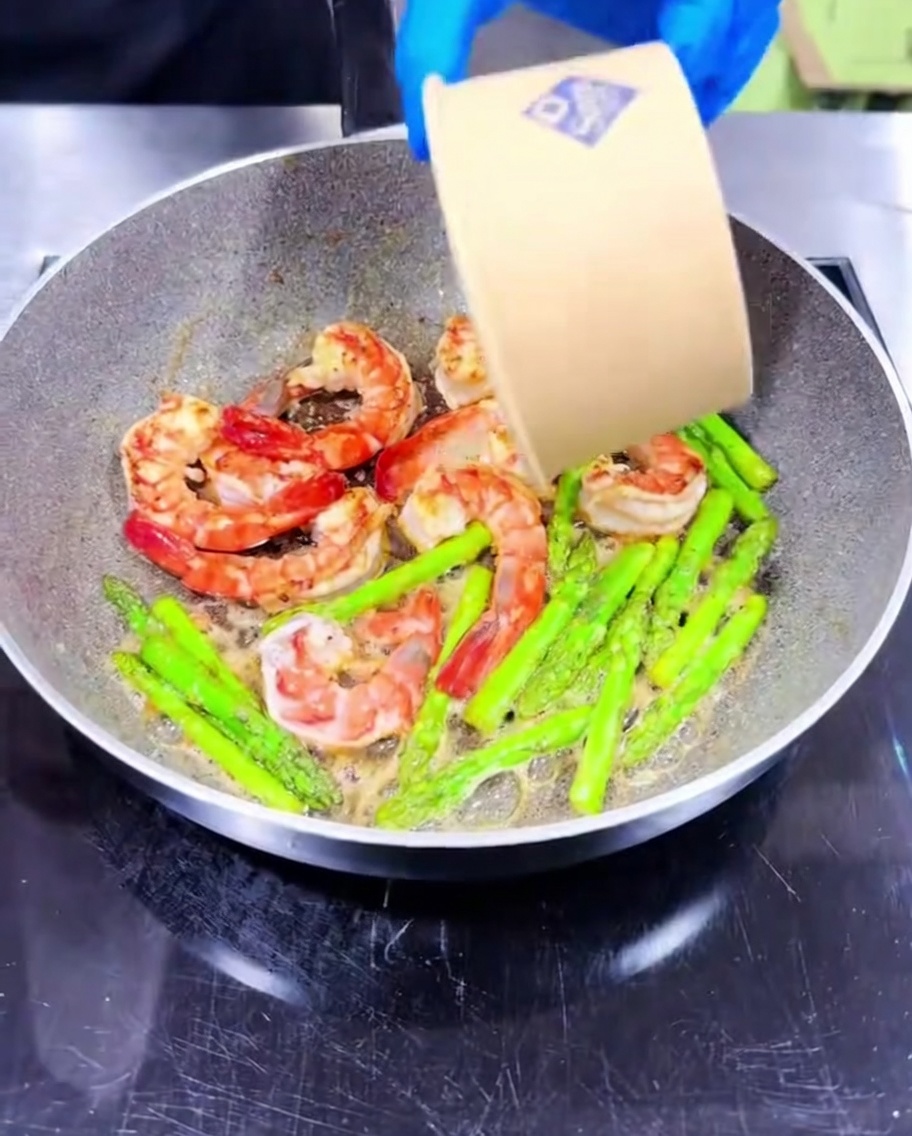 Ajo picado siendo mezclado en la sartén con los camarones y espárragos.