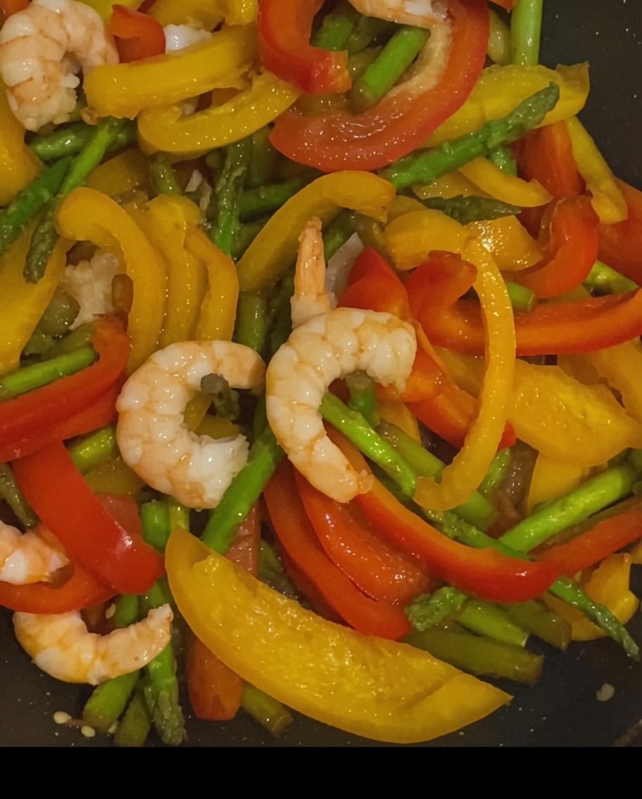 Camarones, pimientos y espárragos salteados, sazonados con granos de pimienta negra en una sartén caliente.