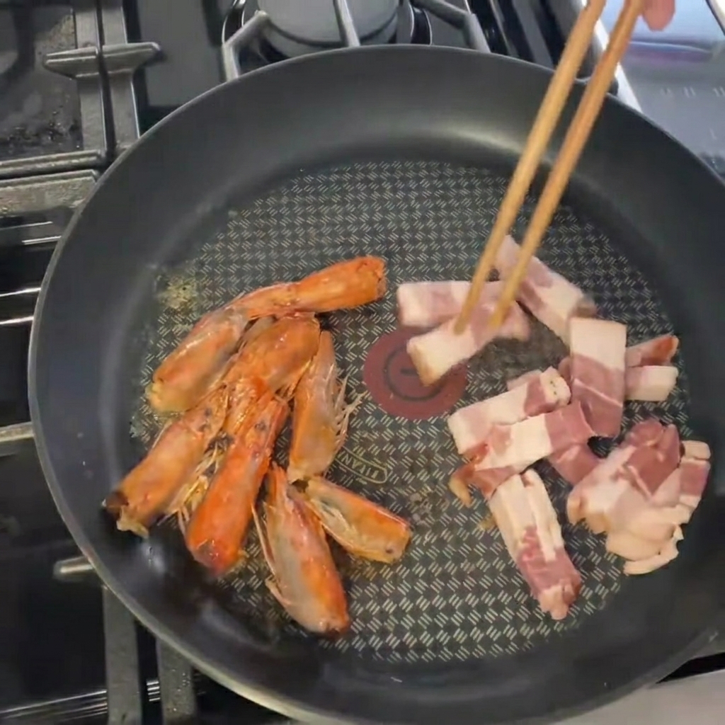Trozos de tocino siendo añadidos a la sartén con las cabezas de camarón.
