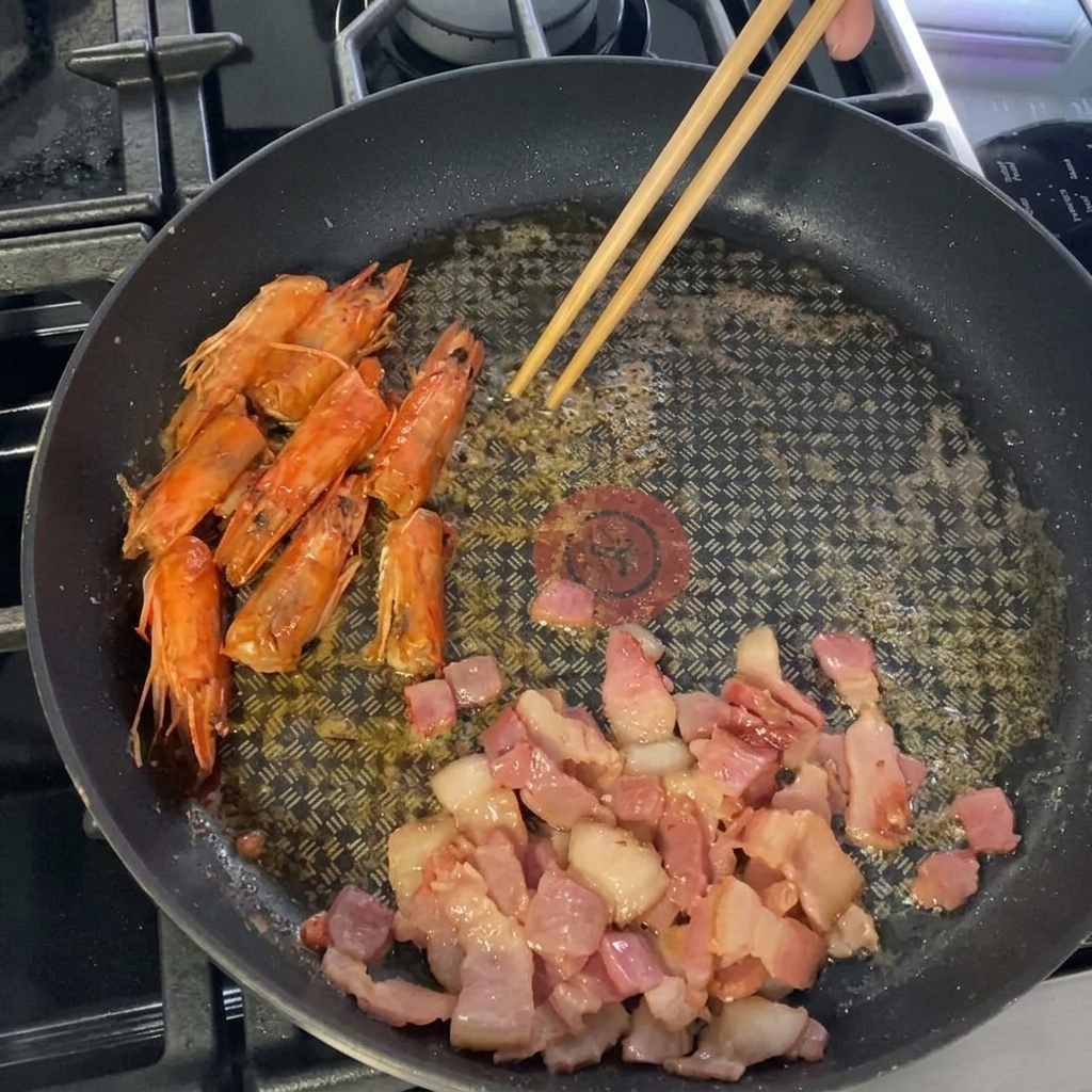 Camarones pelados siendo colocados en la sartén con el tocino.