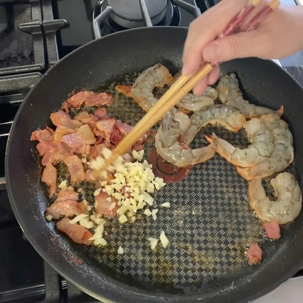 Ajo picado siendo esparcido sobre la mezcla de camarones y tocino.