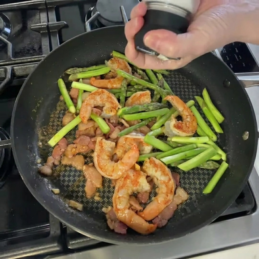 Sazonando la mezcla de camarones y espárragos con sal y pimienta.